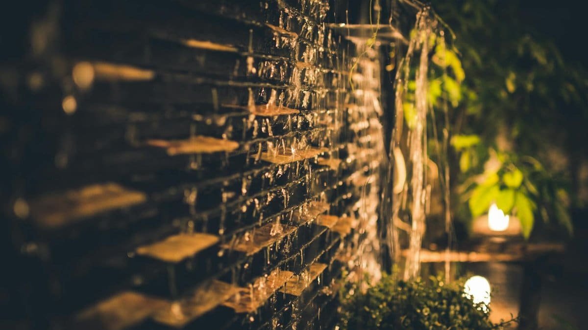 A serene and illuminated garden waterfall captured at night, featuring cascading water over bricks and soft ambient lighting.