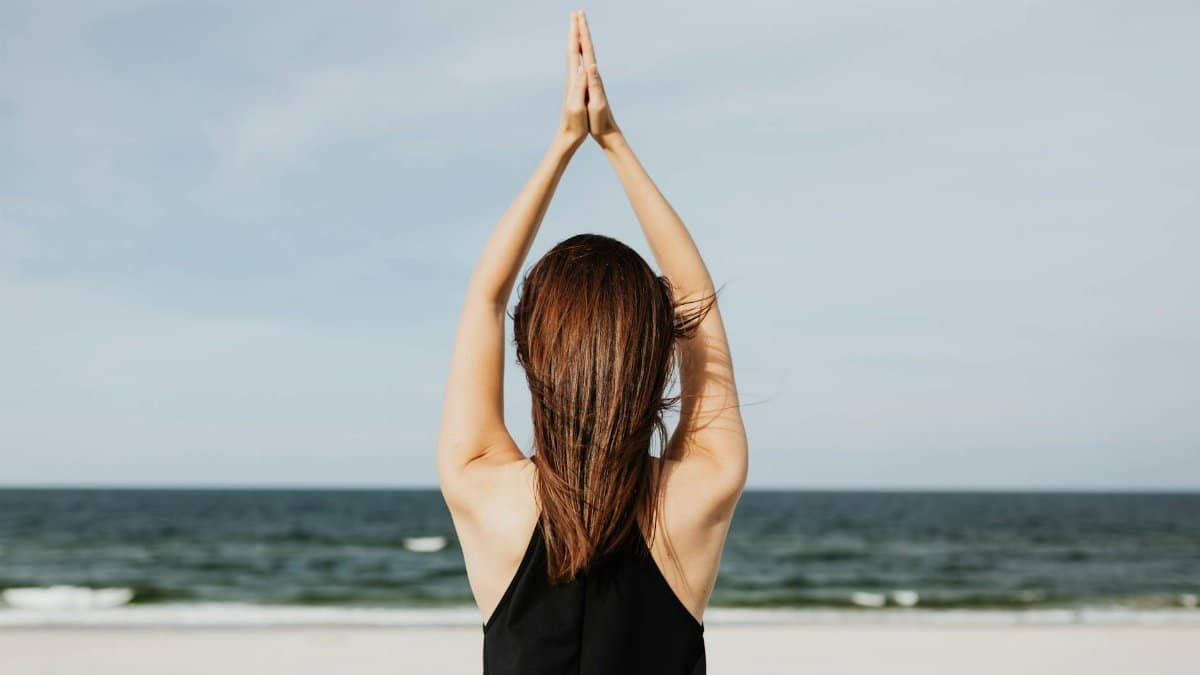 Back view of a woman practicing yoga by the sea, embracing peace and tranquility.