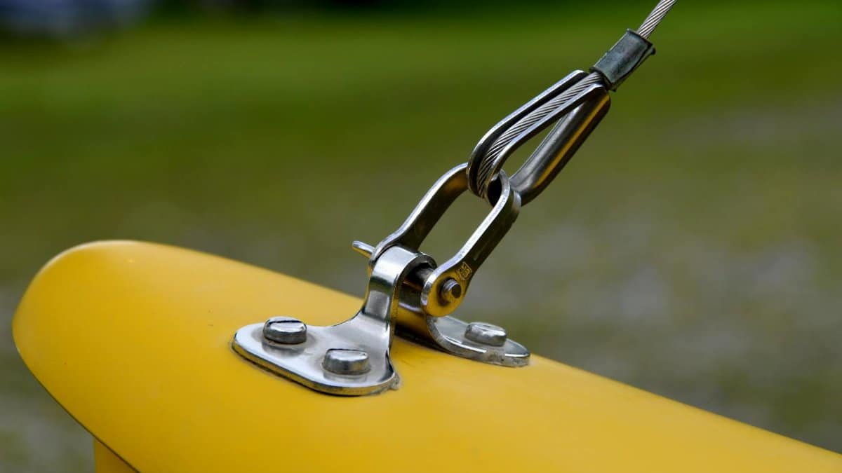 Detailed view of a metal wire rope fastened to a bright yellow surface outdoors.