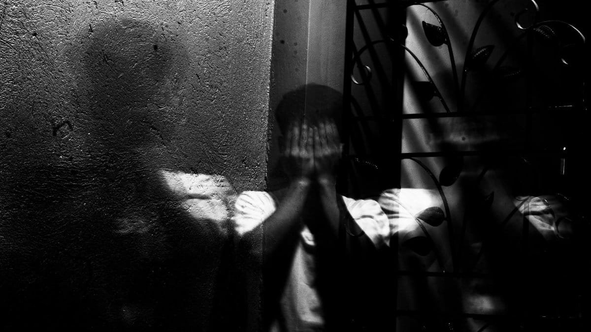 Grayscale image of a man covering his face, evoking themes of fear and introspection.