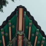 This image captures the vibrant design of a traditional Korean roof structure in Seoul, surrounded by trees.