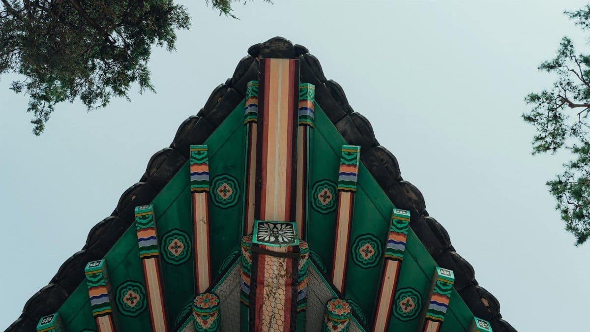 This image captures the vibrant design of a traditional Korean roof structure in Seoul, surrounded by trees.