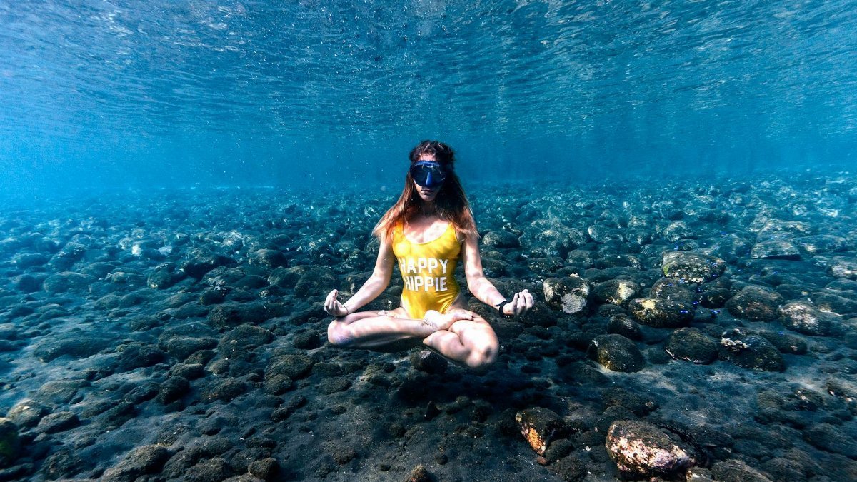 Woman practicing yoga in lotus pose underwater, Bali's serene ocean setting.