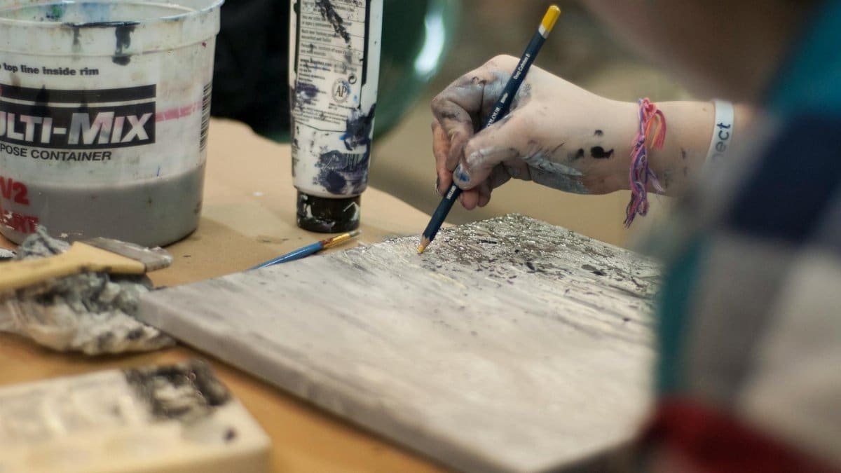 Close-up of an artist's hand painting a textured abstract piece. Creative process in studio.