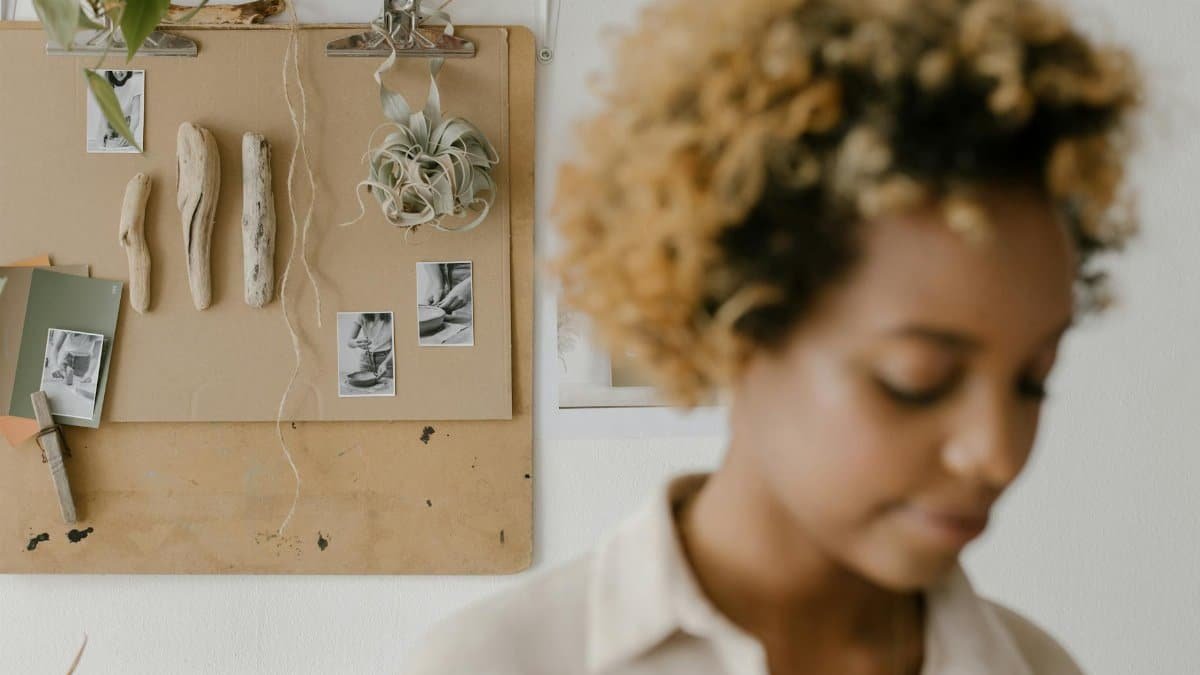 A woman in a workshop with a creative bulletin board displaying art materials and photos.