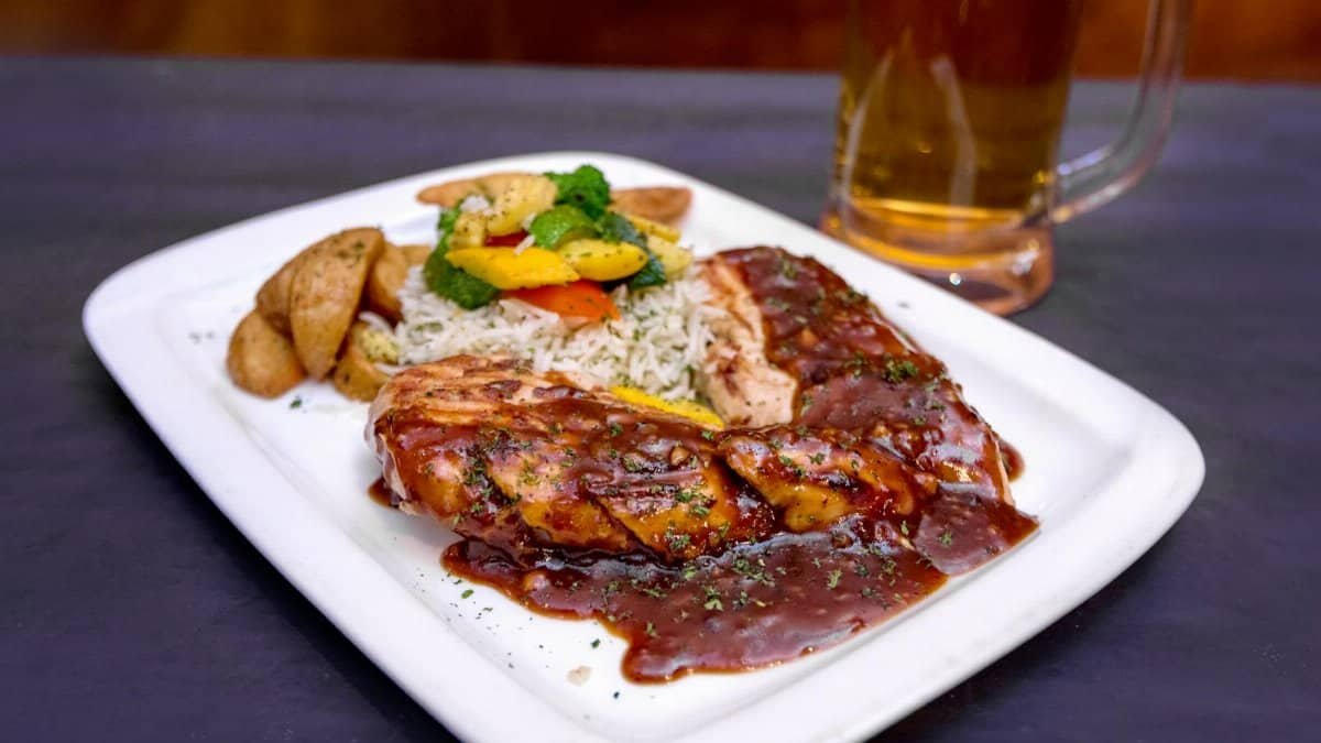 From above of tasty grilled pork steak with barbecue sauce served with salad and fried potato on table near mug of beer