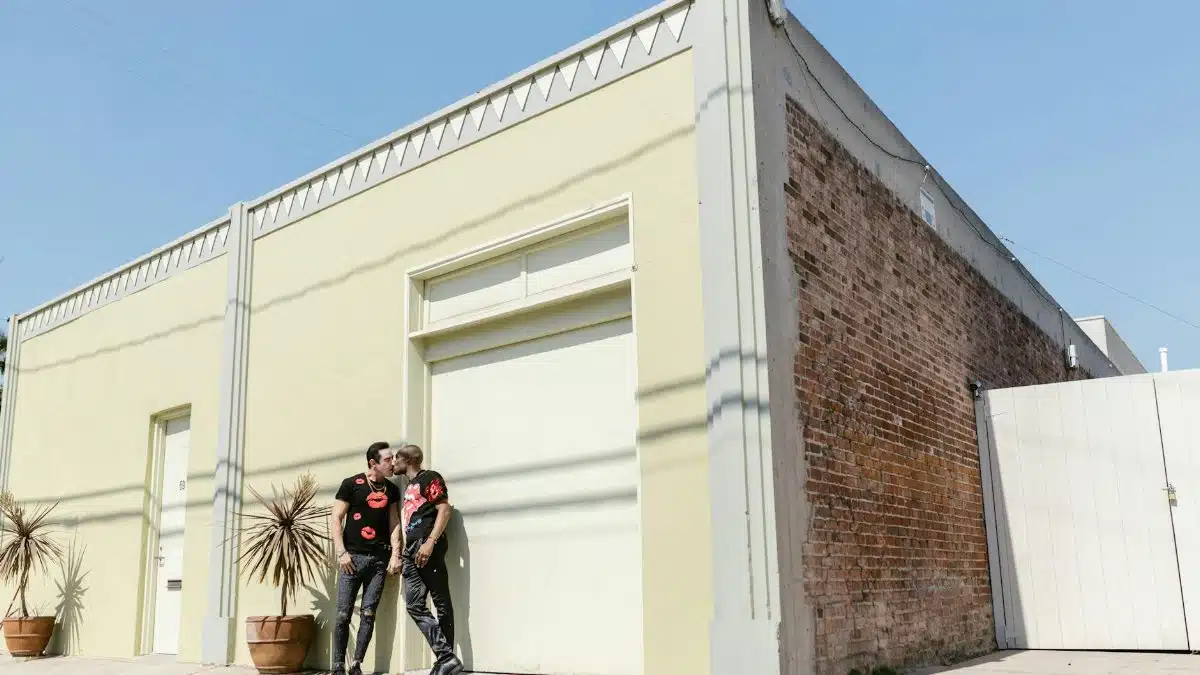 A gay couple expressing love with a kiss in front of an urban building, representing affection and LGBTQ+ pride.