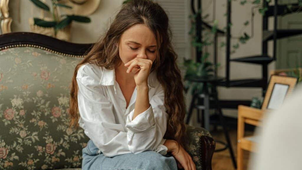Woman in a white shirt sitting thoughtfully on a vintage sofa indoors.