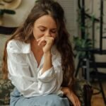 Woman in a white shirt sitting thoughtfully on a vintage sofa indoors.