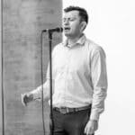 A man sings passionately into a microphone, captured in black and white, evoking a dramatic and classic feel.