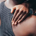 Close-up of a person holding their shoulder, wearing a black sports bra.