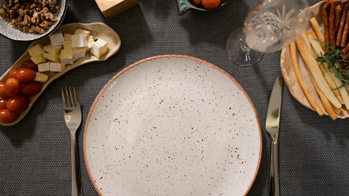 Flat lay of a dinner table with an empty plate, cutlery, and various appetizers like cheese and cherry tomatoes.