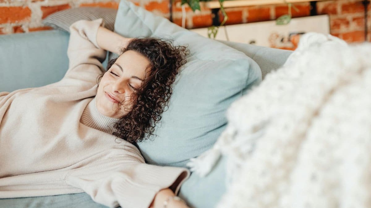 Woman with curly hair relaxing on a comfortable sofa in a cozy indoor setting.