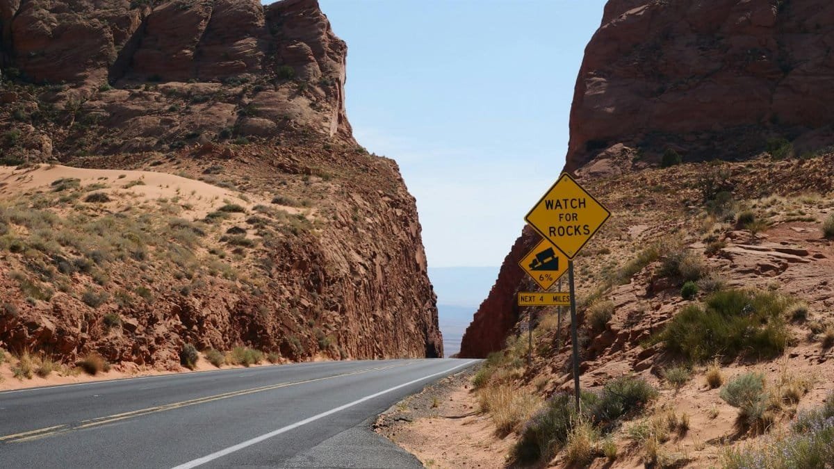 A picturesque road cutting through a rocky desert canyon under a clear blue sky.