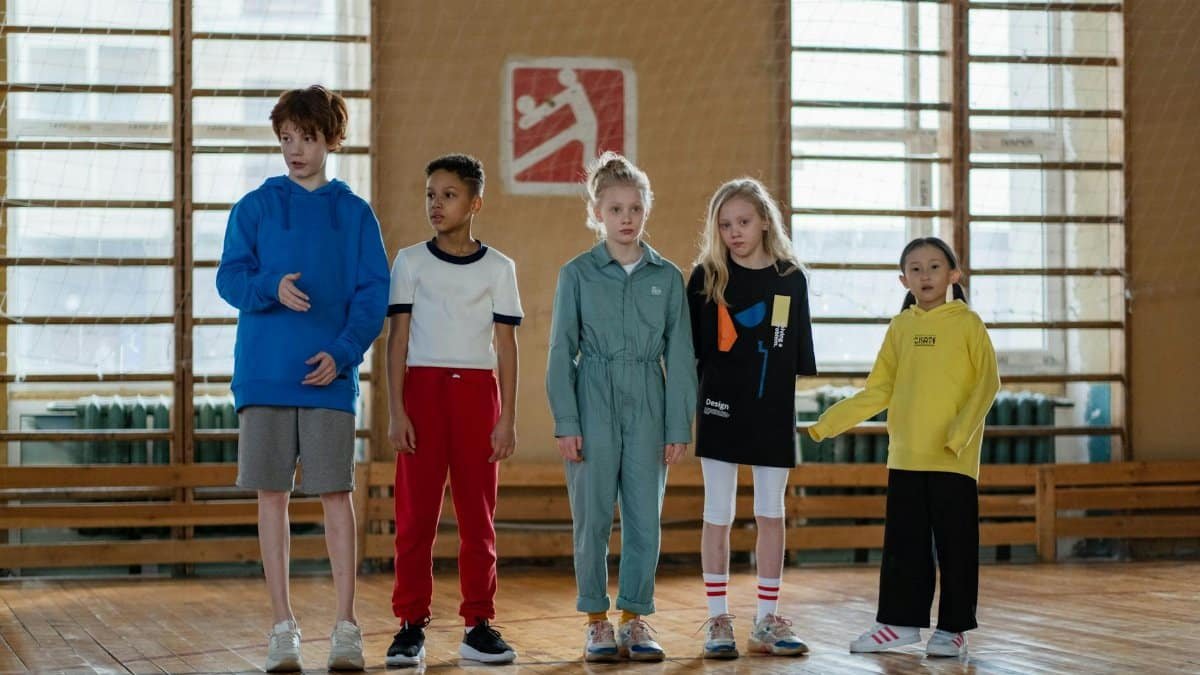 A diverse group of children in a sports hall preparing for an activity, showcasing teamwork and joy.