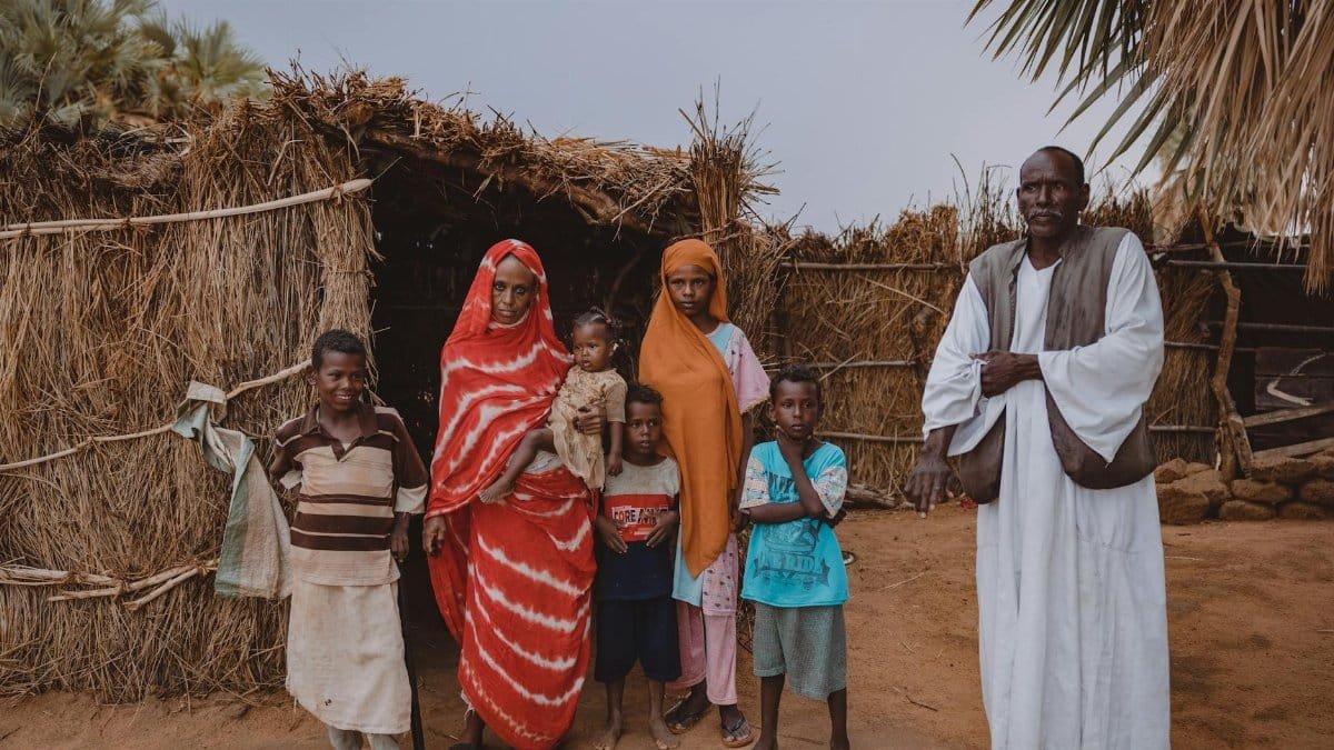 A family stands together outside a traditional thatch-roofed hut in an African village.