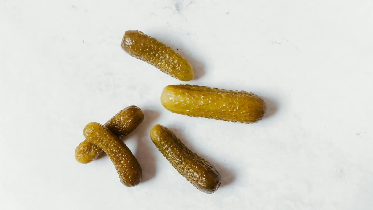 Five pickled cucumbers arranged on a clean white background, emphasizing texture and color.