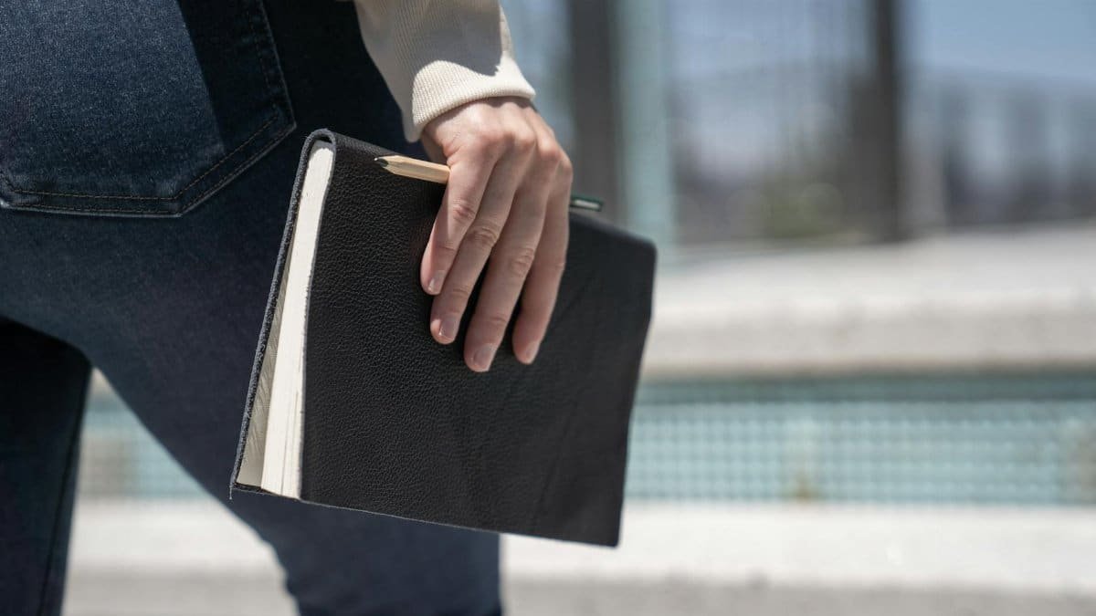 A close-up shot of a woman holding a black hardcover notebook while walking outdoors.