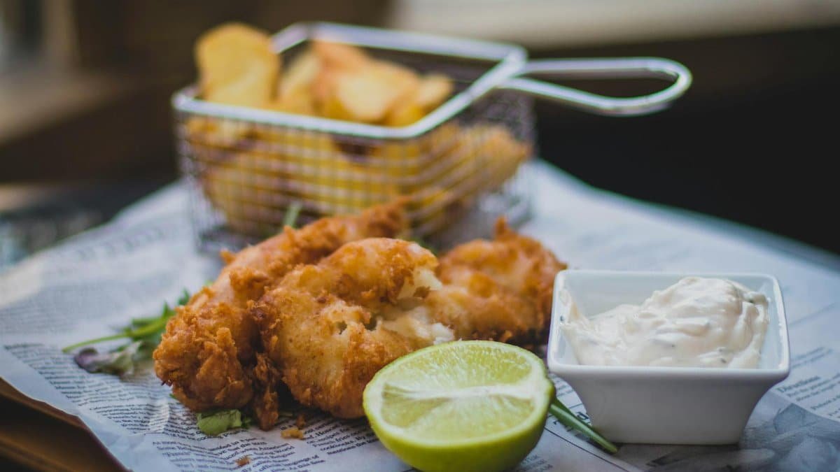 Close-up of fried fish and chips with tartar sauce and lime, perfect for food lovers.