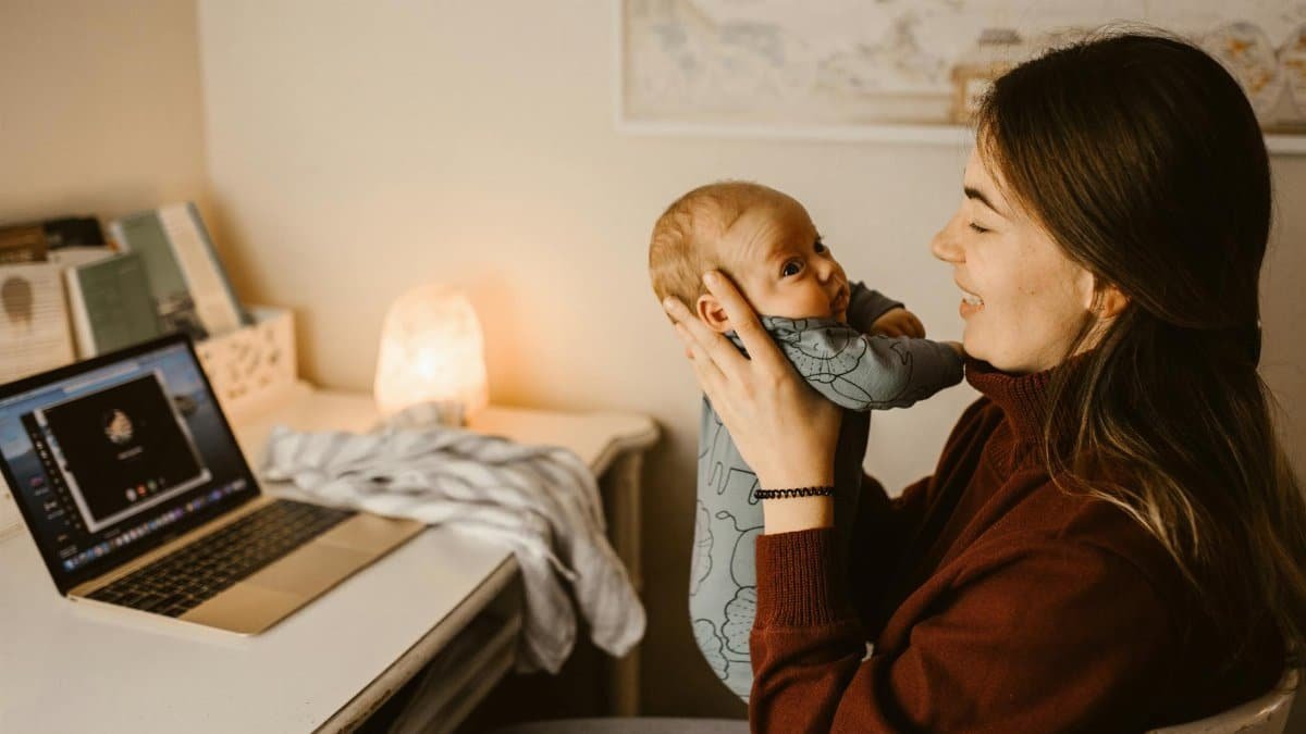 Mother holding baby while video calling from home office. Cozy and heartwarming indoor scene.