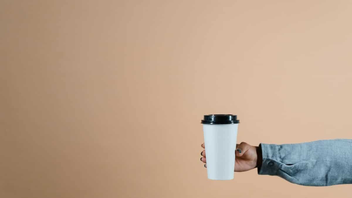 A simple photo of a hand holding a coffee cup against a beige background with copyspace.