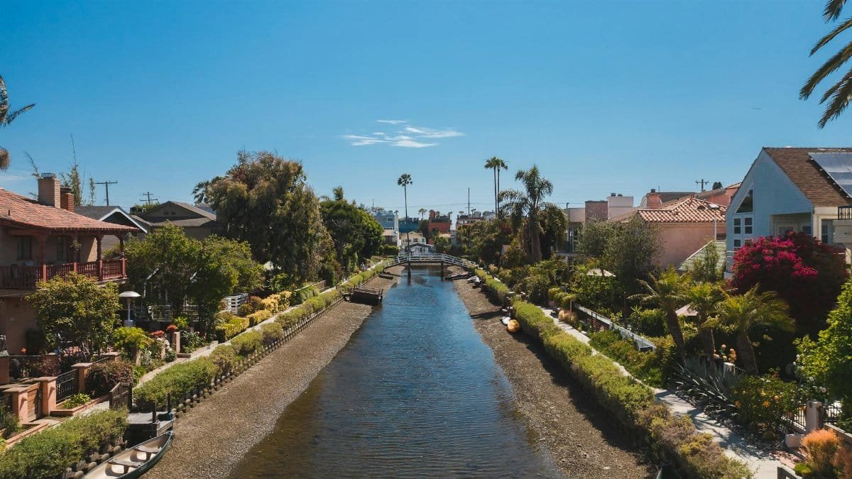 Sunny day view of Venice Canals in Los Angeles with lush gardens and classic architecture.