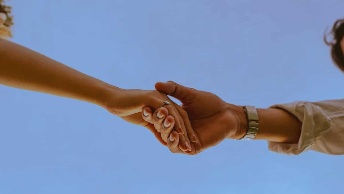 Hands of a couple clasped together with a blue sky background, symbolizing unity and connection.