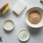 Top view of bowls with ingredients for organic scrub arranged with pumice stone and fresh branches of rosemary