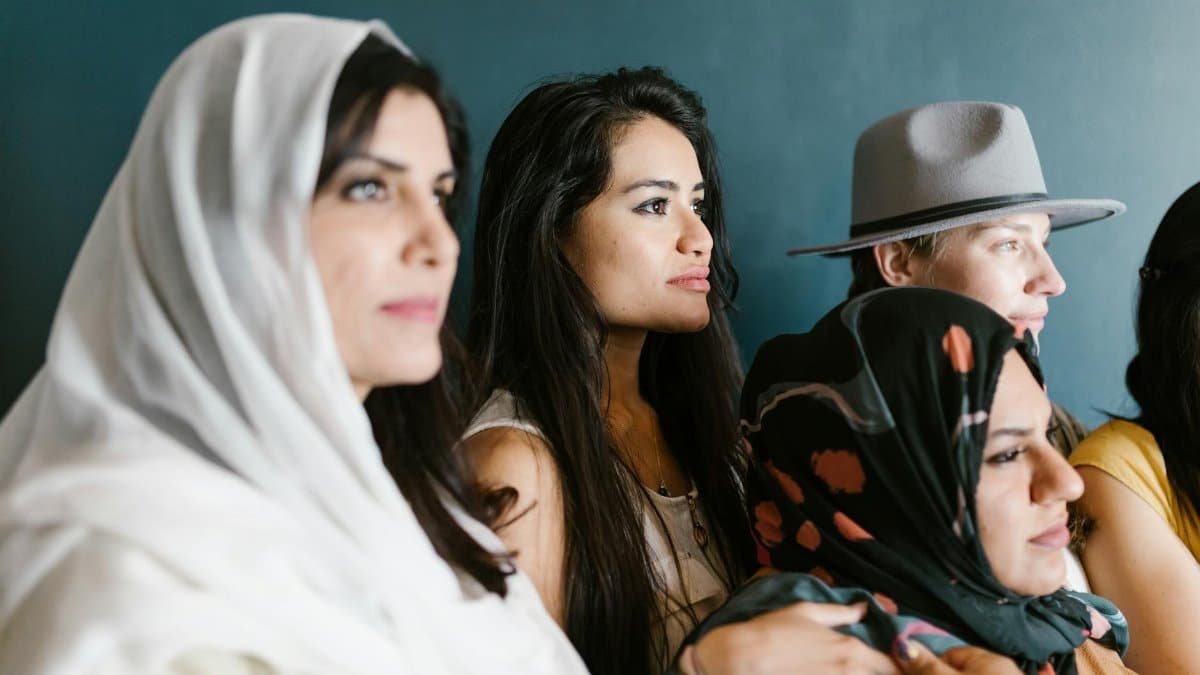 Diverse group of women wearing headscarves and hats, captured in an indoor setting.