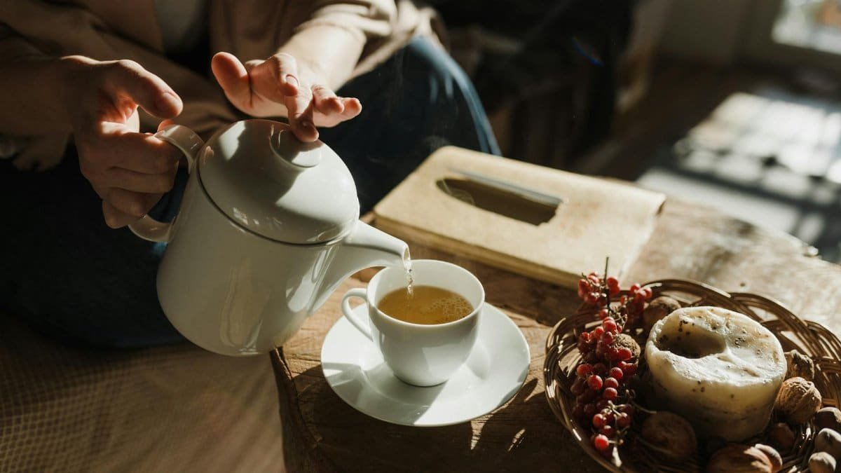 Pouring tea into a cup on a cozy afternoon with warm sunlight filtering indoors.