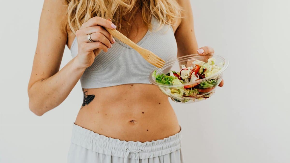 Young woman in sports attire holding a fresh salad bowl, promoting a healthy lifestyle.