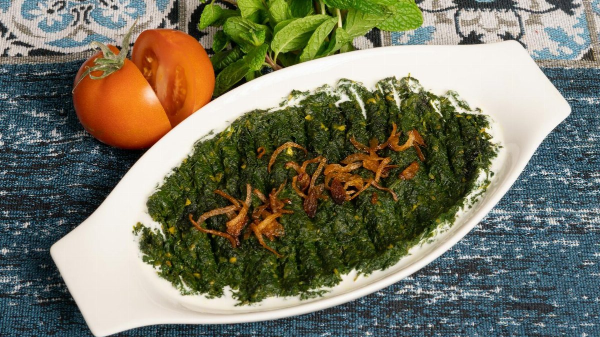 A tasty spinach dish garnished with fried onions, served with fresh tomatoes and mint.