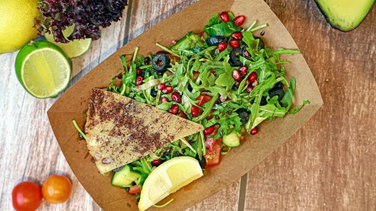 Vibrant salad with arugula, pomegranate, and avocado served with lemon on a wooden table.