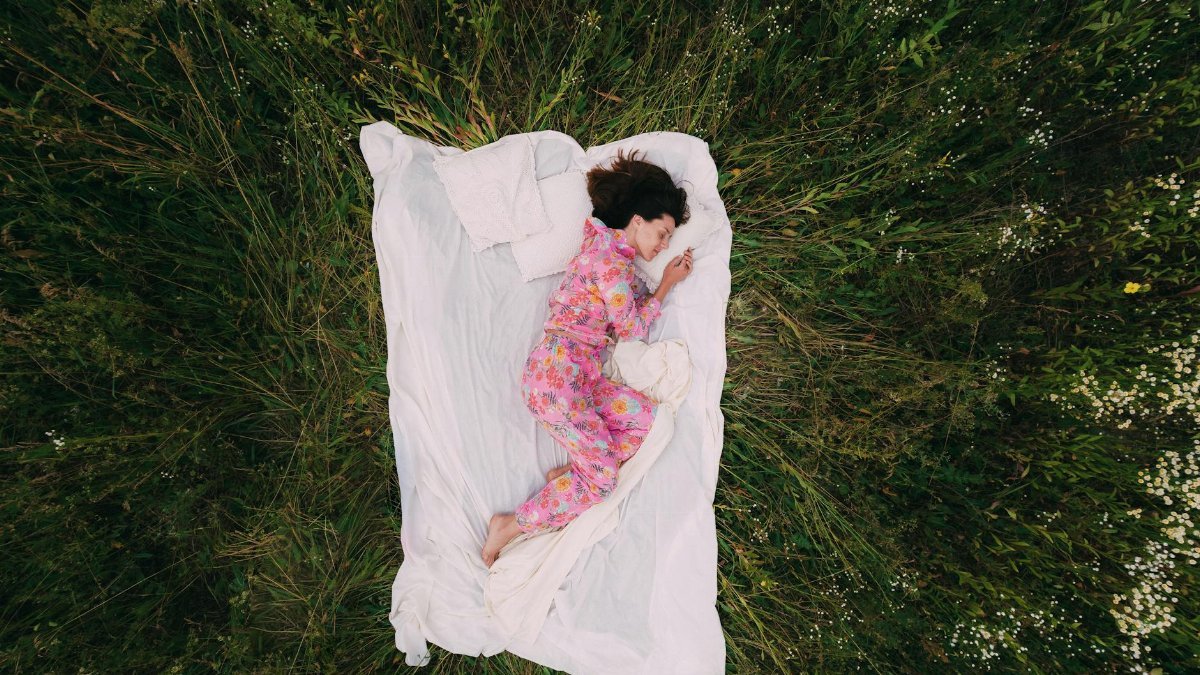 Woman in floral pajamas peacefully napping outdoors on a blanket in a grass field.