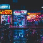 Colorful street scene in Kolkata with glowing shop signs and wet pavement at night.