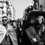 Black and white scene of protesters and police in an Algerian street, highlighting tension.