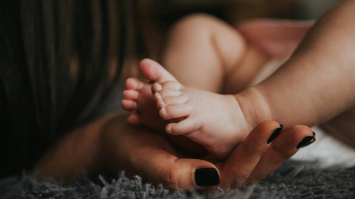 Close-up of a mother's hand gently holding her baby's tiny feet, symbolizing warmth and affection.