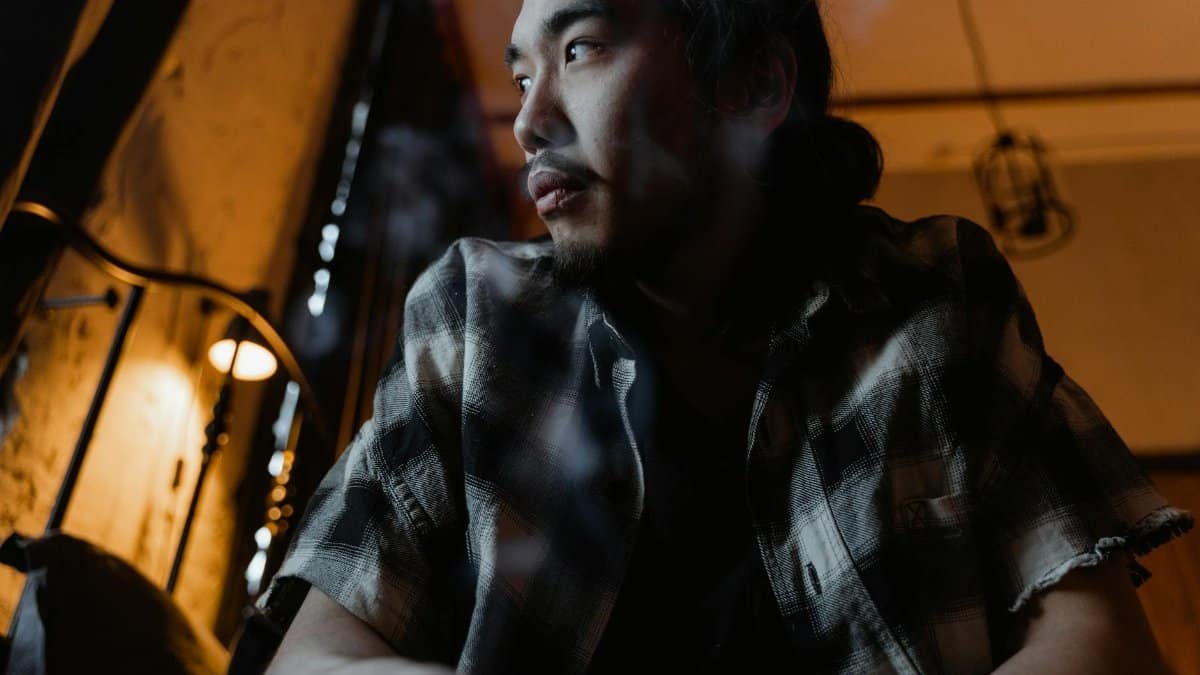 Thoughtful man gazing out in a dimly lit room, reflecting deep emotions.