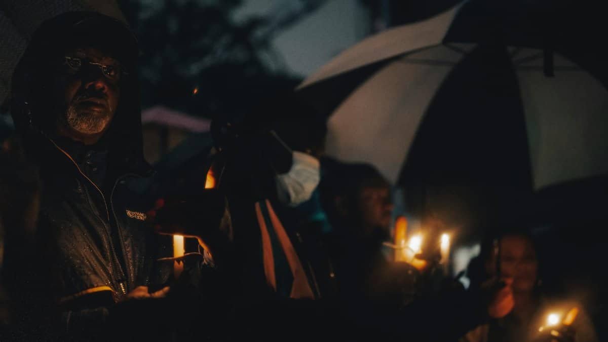 A peaceful candlelight vigil with people holding candles in the evening rain.