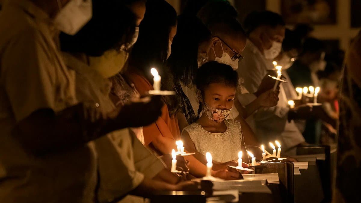 A group participates in a solemn candlelight vigil, wearing masks for safety.