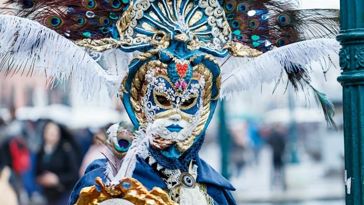Intricate Venetian mask adorned with peacock feathers at a carnival.