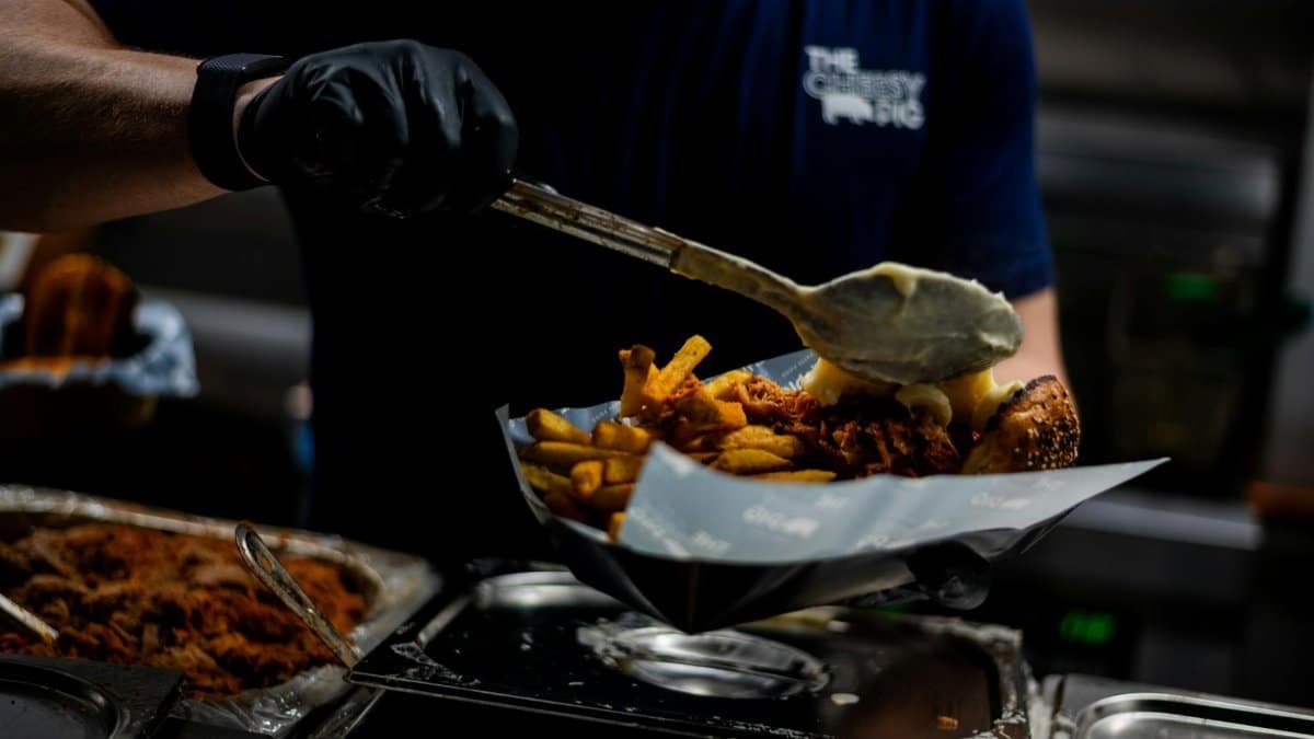 A chef in a street food stall prepares delicious loaded fries with cheese and meat.