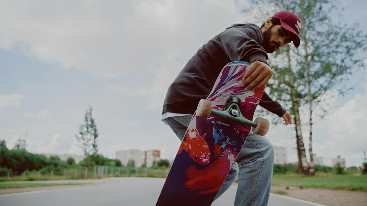 A male skateboarder performing tricks on a colorful board outdoors on a sunny day.