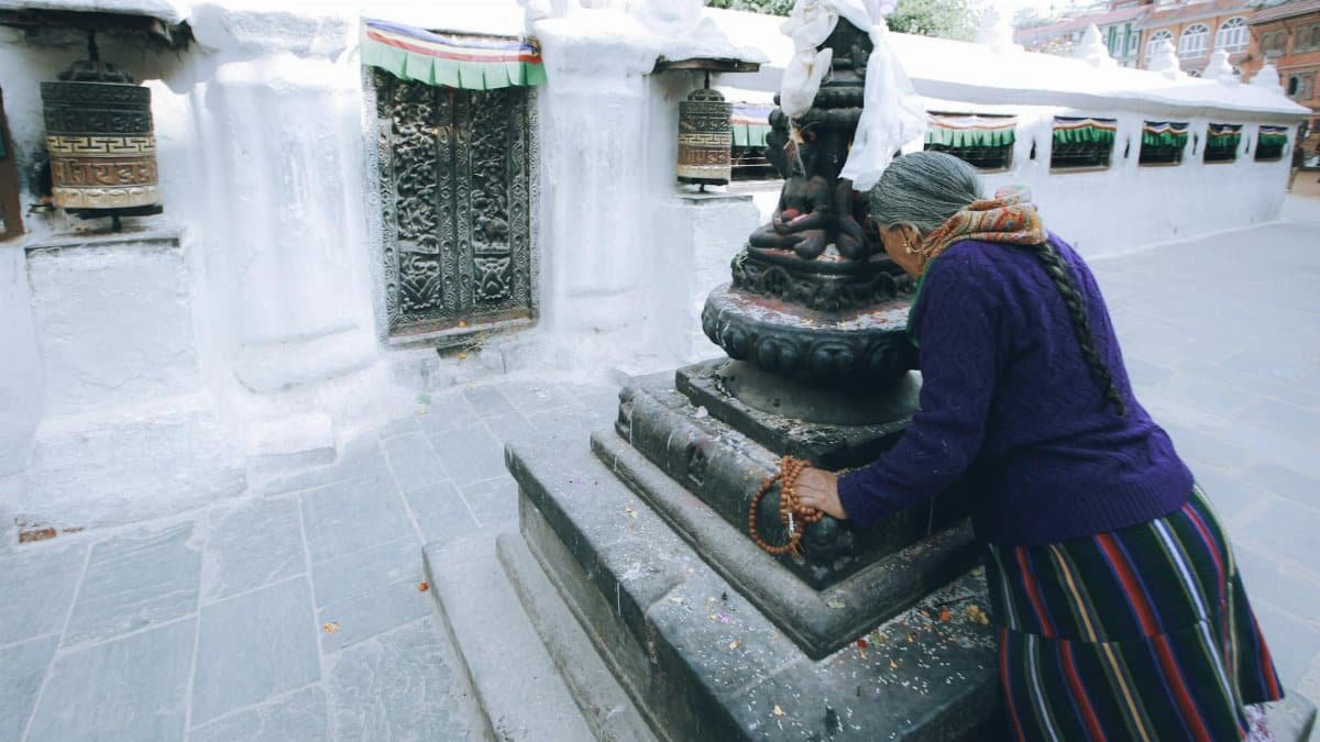 A serene image of an elderly woman praying at a sacred Buddhist site, captured in a traditional setting.
