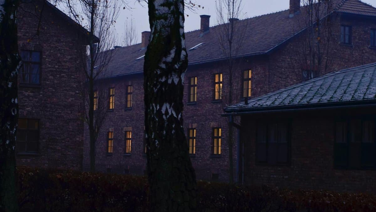 Dark and moody view of Auschwitz buildings and leafless trees, reflecting somber history.
