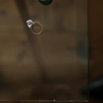 A single engagement ring rests on a glass table, symbolizing relationship reflection.