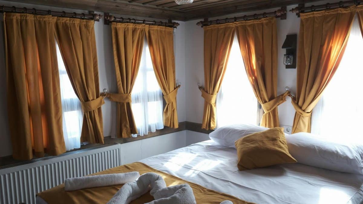 A cozy bedroom in Karabük, Türkiye with warm yellow curtains and sunlight filtering through windows.