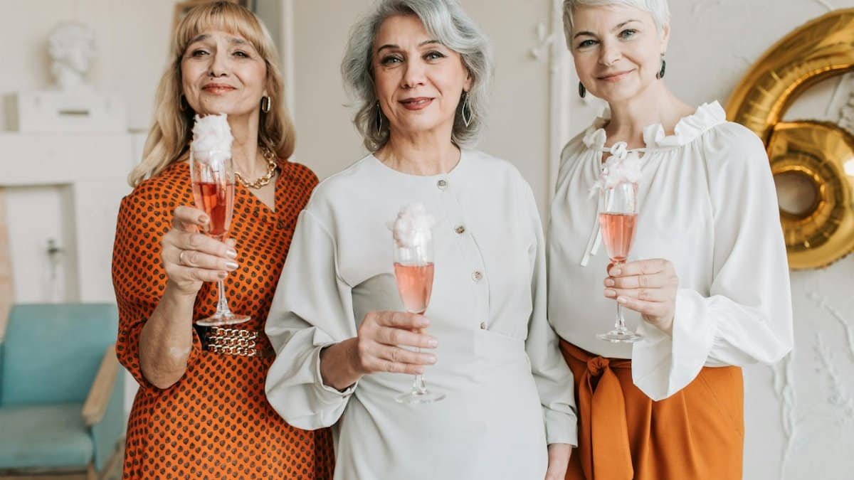 Three senior women smiling and celebrating indoors with champagne glasses, showcasing togetherness.
