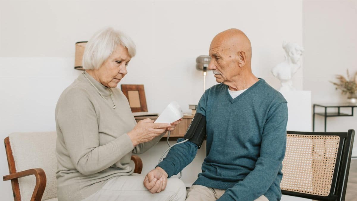 Senior couple measuring blood pressure at home, showcasing care and companionship.