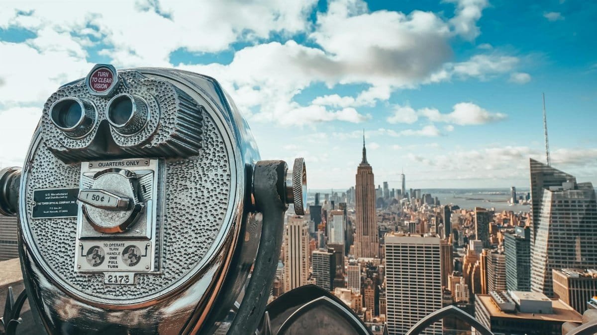 View of New York City skyline featuring iconic Empire State Building with observation binoculars in the foreground.